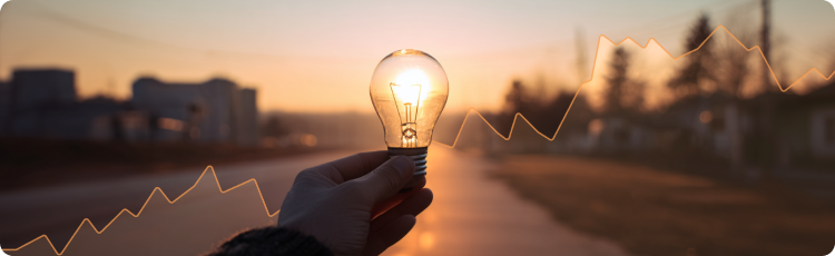 Mano sosteniendo una bombilla luminosa sobre un fondo de atardecer con una gráfica bursátil ascendente superpuesta, simbolizando el potencial de crecimiento y la innovación en las inversiones en acciones de servicios públicos.