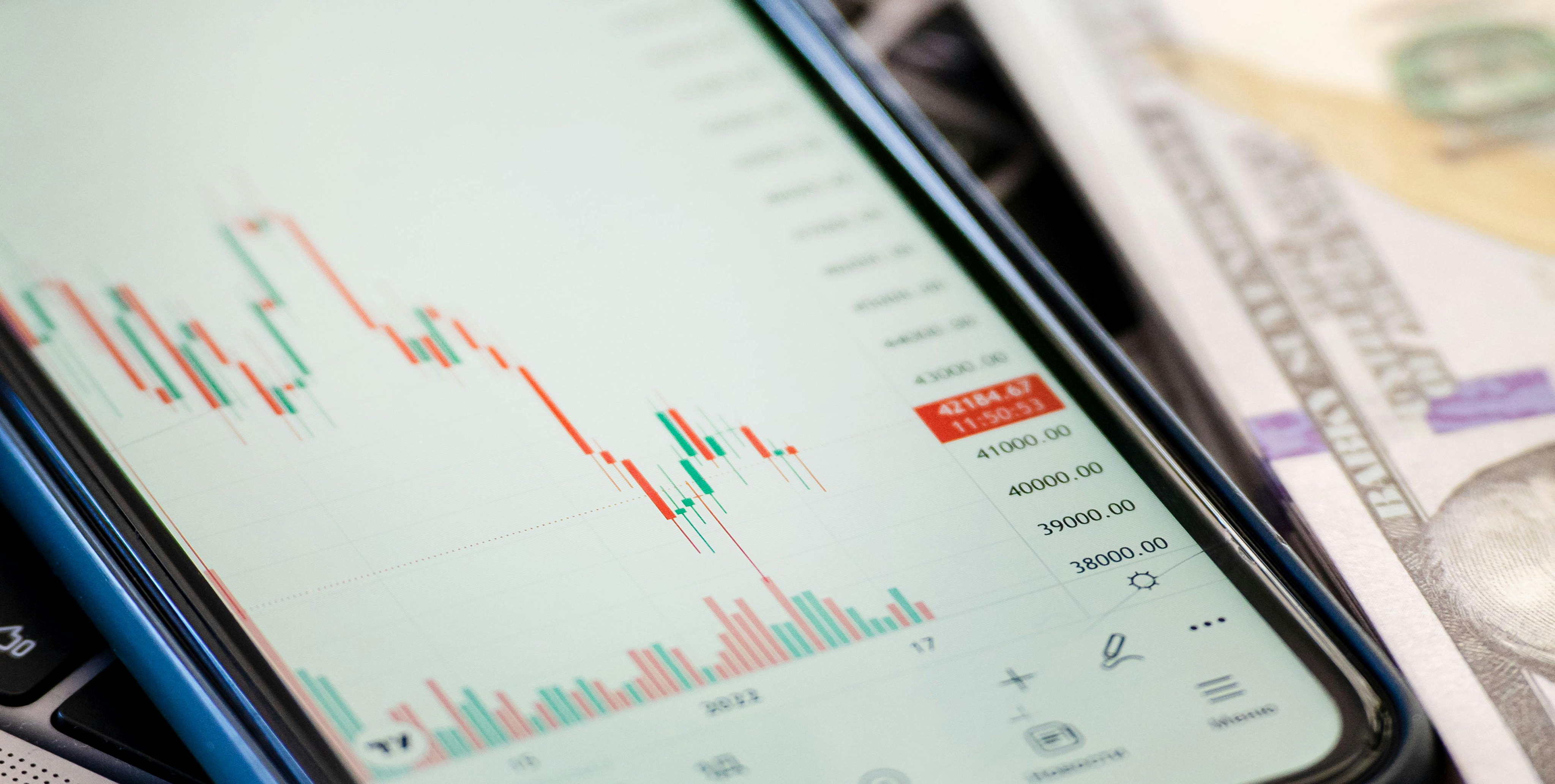 Smartphone a mostrar grÃ¡fico de investimentos em cima de notas de dolar