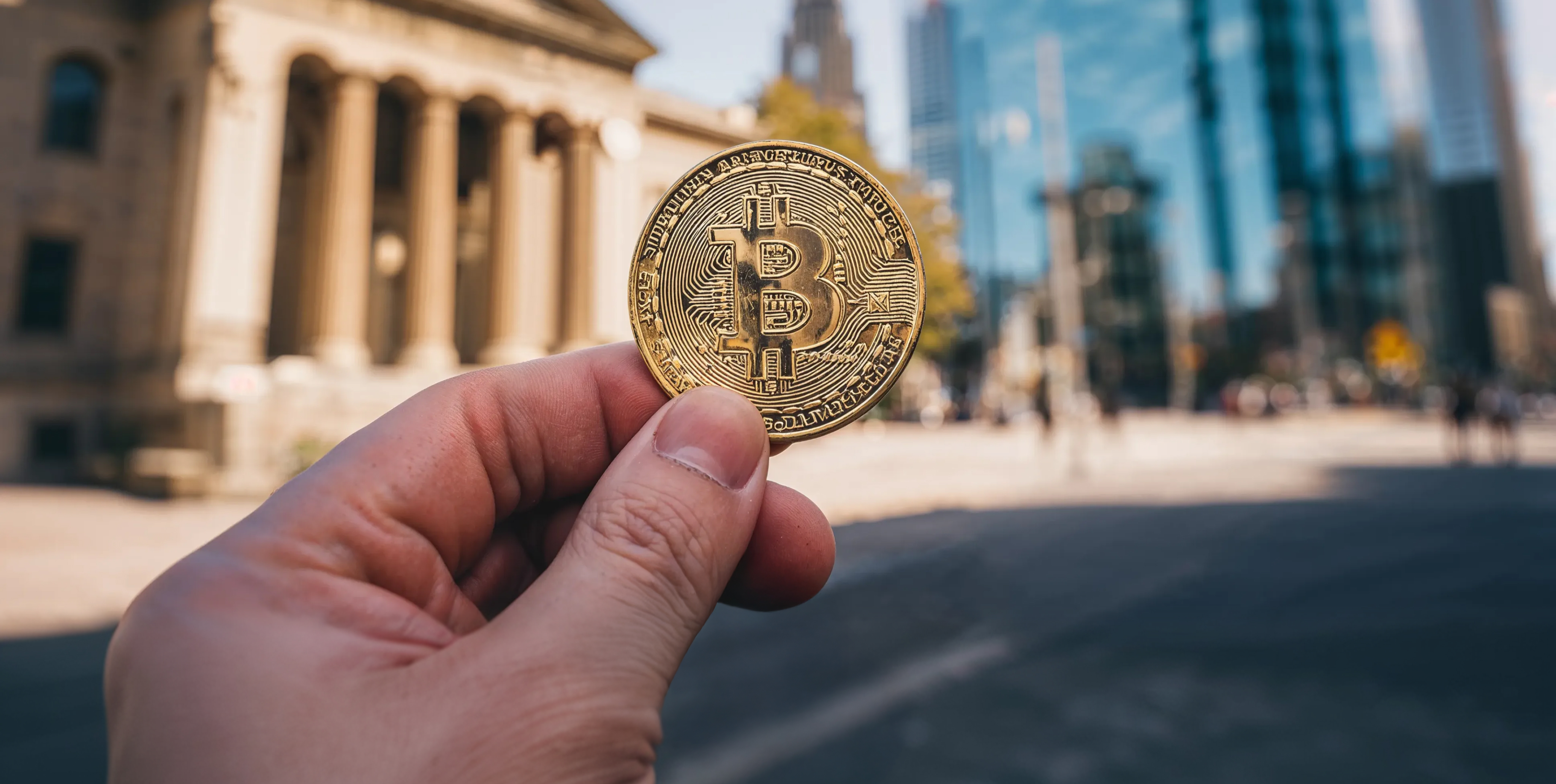 Egy kÃ©z fizikai Bitcoin Ã©rmÃ©t tart egy vÃ¡rosi pÃ©nzÃ¼gyi negyedben, ami a kriptovaluta befektetÃ©st, a digitÃ¡lis eszkÃ¶zÃ¶ket Ã©s a Bitcoin egyre nÃ¶vekvÅ szerepÃ©t szimbolizÃ¡lja a globÃ¡lis piacokon.