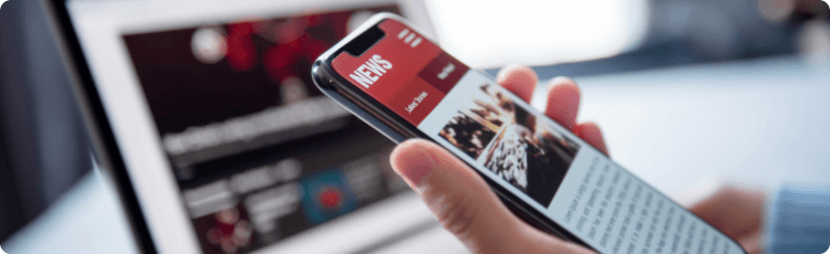 Valaki okostelefonon pÃ©nzÃ¼gyi hÃ­reket olvas egy laptop mellett.