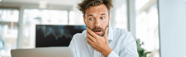 MeglepÅdÃ¶tt ember egy laptop kÃ©pernyÅjÃ©t nÃ©zi, mikÃ¶zben a hÃ¡ttÃ©rben elmosÃ³dott kereskedÃ©si grafikon lÃ¡thatÃ³.