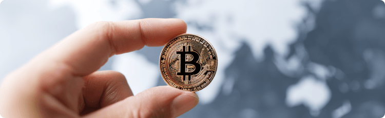  Ruka drÅ¾iaca bitcoinu na rozmazanej mape sveta, ilustrujÃºca globÃ¡lne prijatie kryptomien a medzinÃ¡rodnÃ© trhy s digitÃ¡lnymi aktÃ­vami.