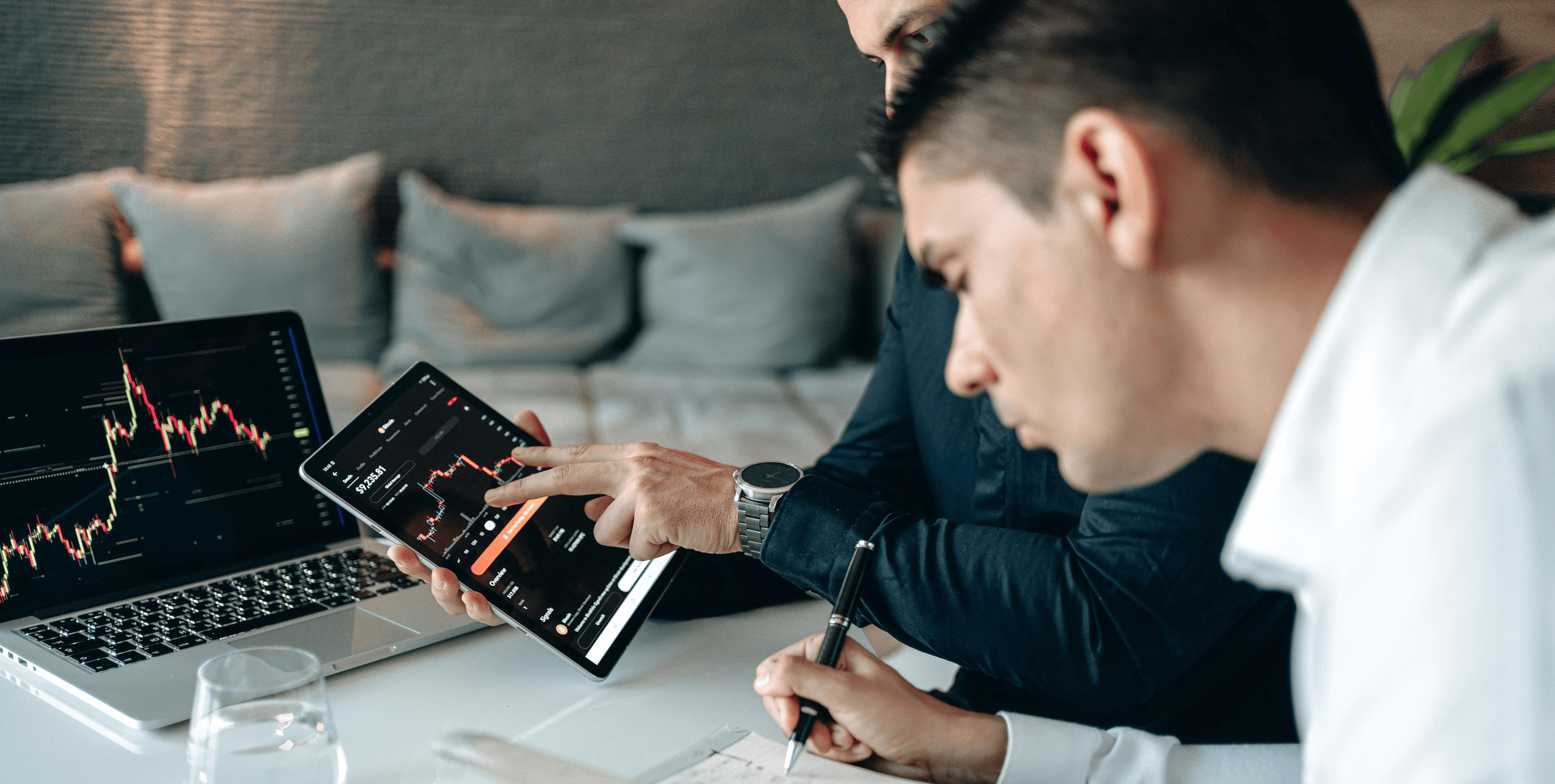 Dois homens a analisar grÃ¡ficos de investimento em laptop e tablet