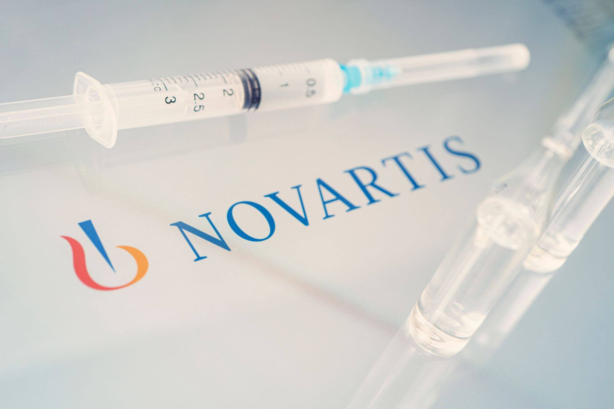 Imagen en la que se ve el logo de Novartis rodeado de varias jeringuillas
