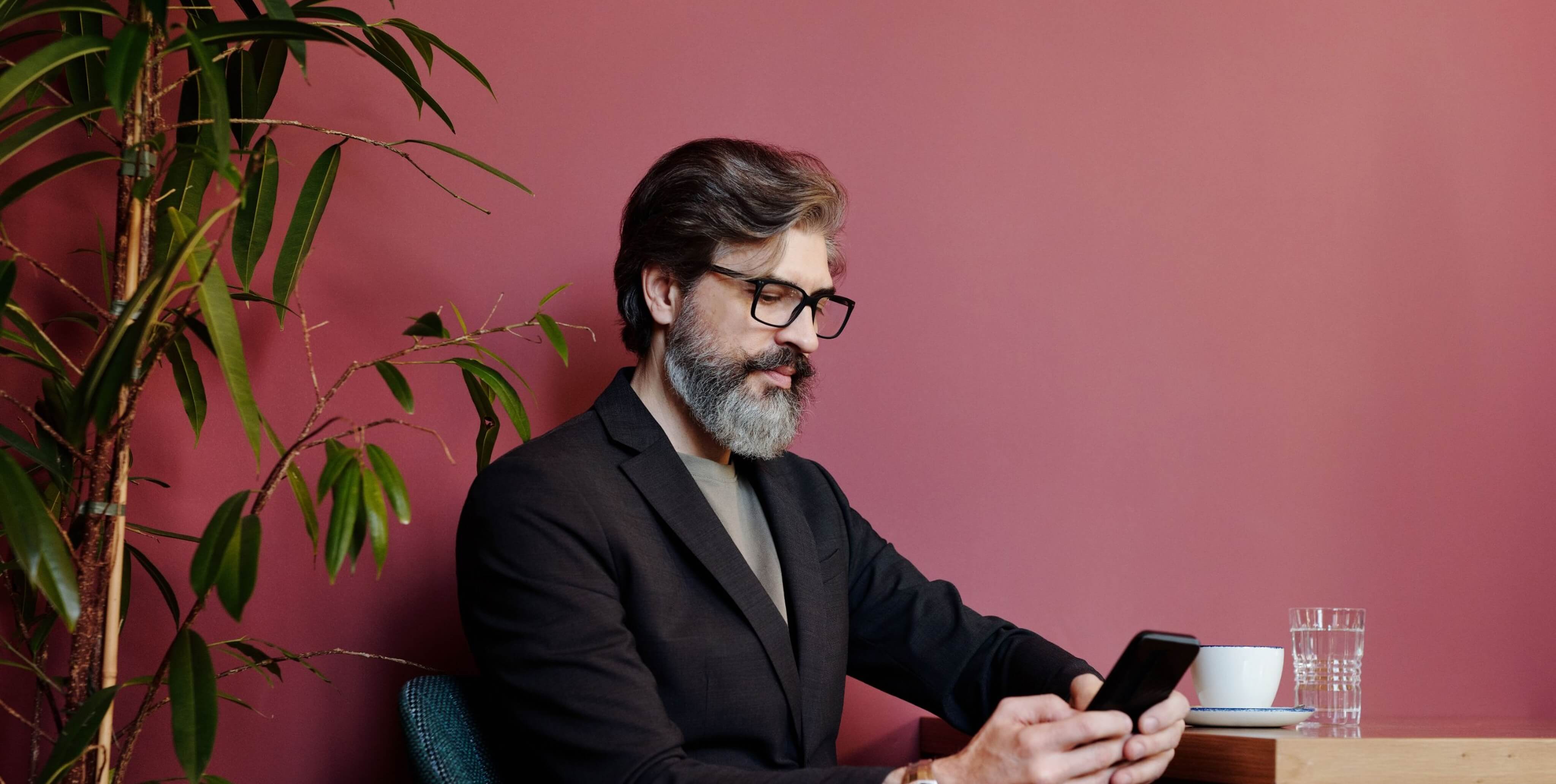 Investidor de barba, óculos e fato a ver o telemóvel