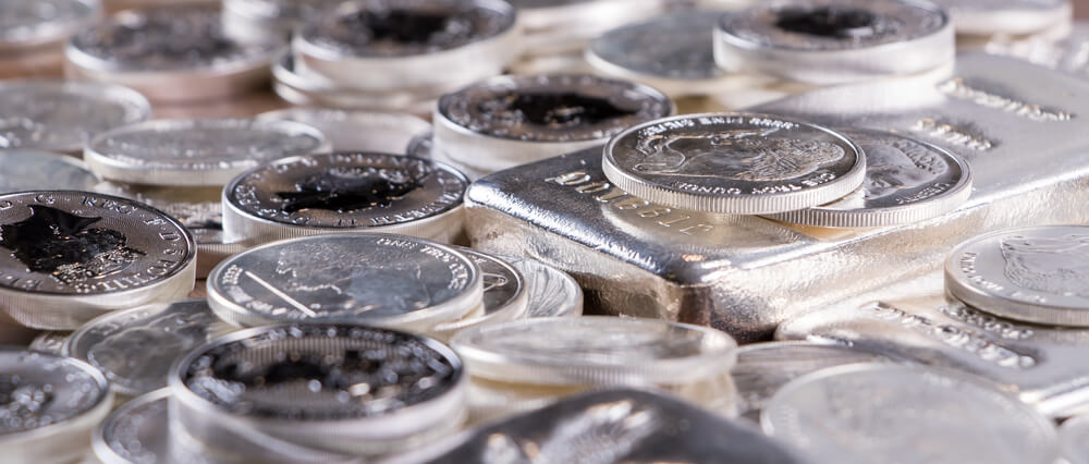 Cierre de barras de plata y monedas de plata apiladas sobre mesa de madera